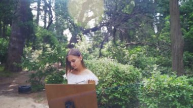 Parkta Kız sanatçı yağlı boyalar küçük bir eski gölet 4k ile bir manzara boyar