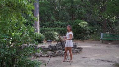 Parkta Kız sanatçı yağlı boyalar küçük bir eski gölet 4k ile bir manzara boyar