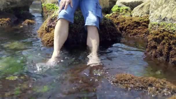 男人的脚被海浪冲走了 那家伙赤脚站在一块石头海岸上 踢与海水和浮动海藻4K — 图库视频影像