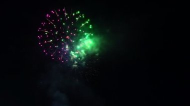 Şehrin üzerinde şenlikhavai. İnsanların neşeli çığlıkları. Gece şehir üzerinde siyah gökyüzünde parlak havai fişek gösterisi. Kırmızı patlamalar karanlıkta renkli parlaklık 4k kıvılcımlar