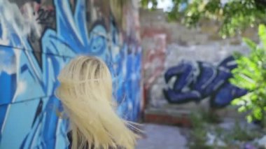 Genç sarışın kız grafitti ile bir duvar arka plan karşı poz. Video oturumu. yavaş çekim