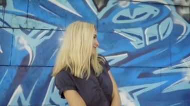 Genç sarışın kız grafitti ile bir duvar arka plan karşı poz. Video oturumu. yavaş çekim