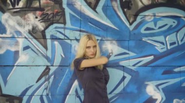 Genç sarışın kız grafitti ile bir duvar arka plan karşı poz. Video oturumu. yavaş çekim