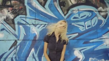 Genç sarışın kız grafitti ile bir duvar arka plan karşı poz. Video oturumu. yavaş çekim