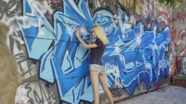 Genç sarışın kız grafitti ile bir duvar arka plan karşı poz. Video oturumu. yavaş çekim