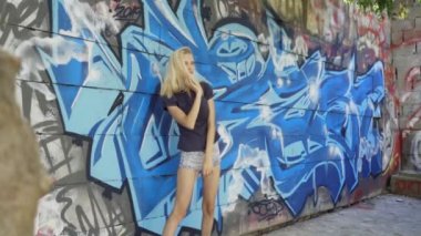 Genç sarışın kız grafitti ile bir duvar arka plan karşı poz. Video oturumu. yavaş çekim