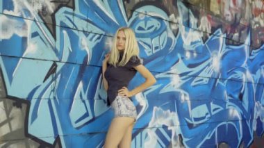 Genç sarışın kız grafitti ile bir duvar arka plan karşı poz. Video oturumu. yavaş çekim