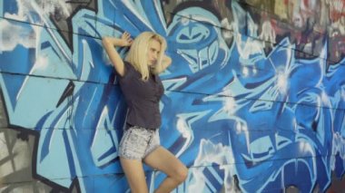 Genç sarışın kız grafitti ile bir duvar arka plan karşı poz. Video oturumu. yavaş çekim