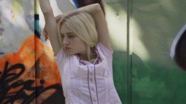 Genç sarışın kız grafitti ile bir duvar arka plan karşı poz. Video oturumu. yavaş çekim