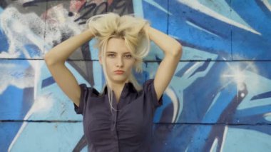 Genç sarışın kız grafitti ile bir duvar arka plan karşı poz. Video oturumu. yavaş çekim