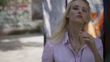 Genç sarışın kız grafitti ile bir duvar arka plan karşı poz. Video oturumu. yavaş çekim