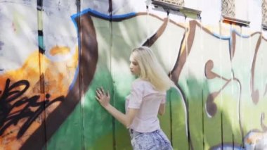 Genç sarışın kız grafitti ile bir duvar arka plan karşı poz. Video oturumu. yavaş çekim. Sallayarak kamera ile canlı çekim