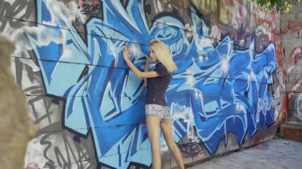 年轻的金发女孩摆姿势的背景与格拉菲蒂的墙壁 视频会话 慢动作 — 图库视频影像