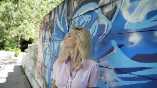 グラフィティと壁の背景にポーズをとる若いブロンドの女の子 ビデオセッション スローモーション 揺れるカメラでライブ撮影 — ストック動画