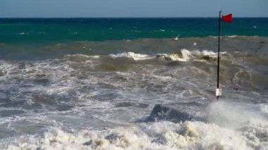 Güneşli havalarda denizde fırtına. Güçlü rüzgar. Yeşil-mavi deniz suyu, güçlü bir rüzgarda uçan martılar. Kırmızı bayrak uyarısı yüzmek yasaktır. 4k