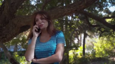 Mavi elbiseli kız mutlu bir şekilde telefonda konuşuyor, gülümsüyor. Parkta telefonda konuşuyorum. 4k