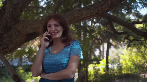 青いドレスを着た女の子は楽しそうに電話で話し 微笑む 公園で電話で話してる4K — ストック動画