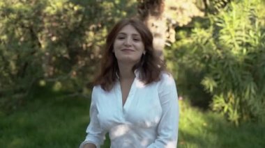 Güzel kız yakın çekim. Parkta beyaz gömlekli kameraya poz veren kız. Gür saçlar. 
