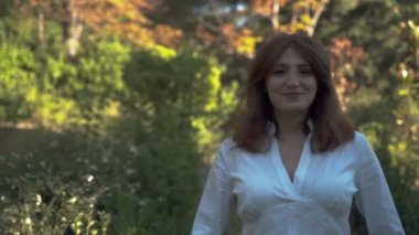 Güzel kız yakın çekim. Parkta beyaz gömlekli kameraya poz veren kız. Gür saçlar. 