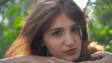 Güzel kız yakın çekim. Parkta beyaz gömlekli kameraya poz veren kız. Gür saçlar. 4k
