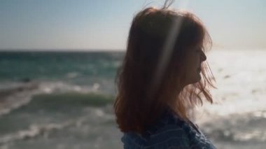 Güzel kız yakın çekim. Kız güçlü rüzgar ve dalgalar ile denizin bir arka plan üzerinde mavi bir elbise kamera için poz lar. Gür saçlar.