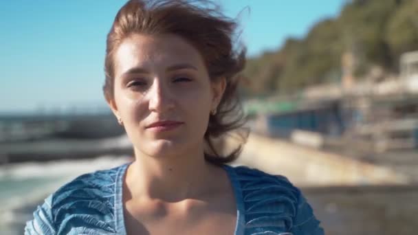클로즈업입니다 소녀는 바람과 파도와 바다의 배경에 파란색 드레스에 카메라를 포즈를 — 비디오