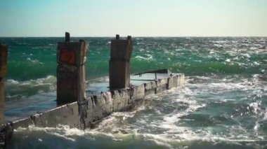Güneşli havalarda denizde güçlü fırtına. Yavaş çekim. Güçlü rüzgar, denizde mavi-yeşil su. Denizde kırık iskele