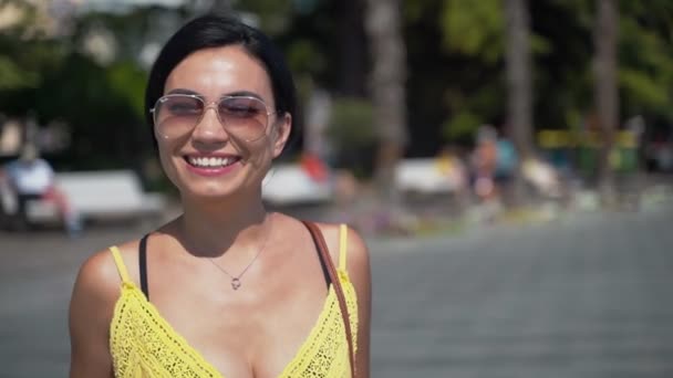 Mädchen schickt einen Luftkuss. Schöne junge brünette Mädchen in einem gelben Kleid und Sonnenbrille Nahaufnahme lächelt und sendet Luftküsse — Stockvideo