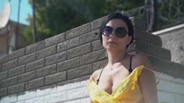 Genç ve güzel bir kız orta parmaklarını gösteriyor. Sarı elbiseli ve güneş gözlüklü güzel esmer kız kamerayı açıp orta parmağını gösteriyor.