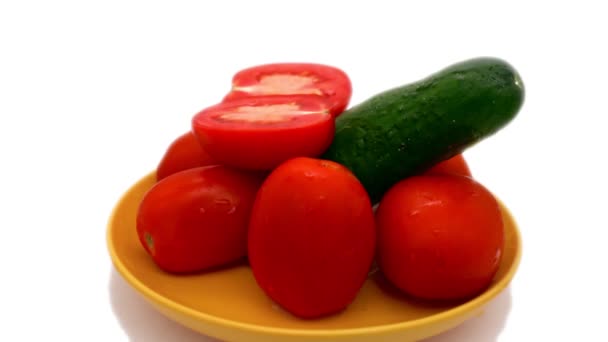 A cucumber stands surrounded by a tomato on a yellow saucer and rotates on a white background. 4k — Stock Video