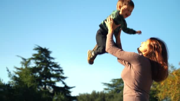 A young mother with a two year old son walks in the city. Sunny warm day in the fall. Mom throws her son up, the son rejoices and laughs. — Stock Video