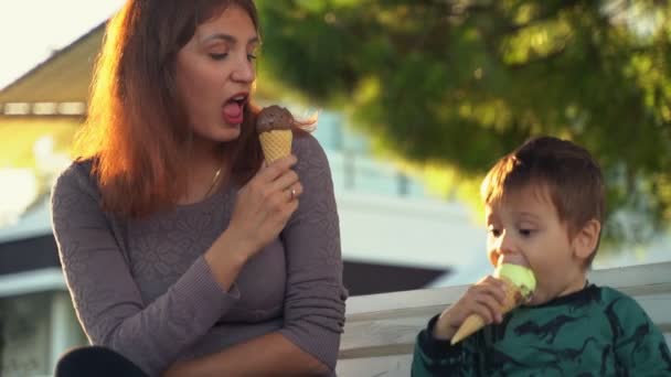 Mam met zoon die ijs eet. Mam en kind. Een jongen die ijs eet. Een kleine jongen met zijn moeder op de bank eet ijs, maar het kind wil ijs ruilen met zijn moeder. — Stockvideo