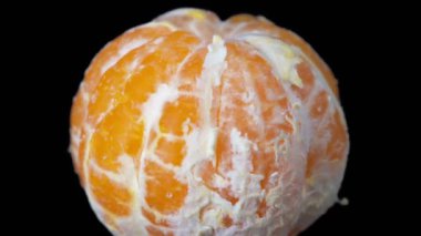 Soyulmuş bir mandalina siyah arka planda döner. Yakın plan..