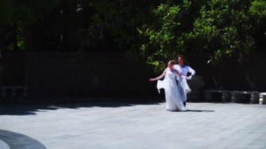 Genç bir adam ve bir kız vals yapıyorlar. Bir öğrenci ve beyaz balo elbisesi giymiş bir kız parkta dans ediyorlar. Yavaş çekimde vals dansı.