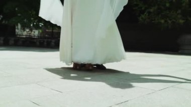 Dans eden bir erkek ve bir kızın bacakları. Üniformalı bir adam ve beyaz elbiseli bir kız parkta ağır çekimde vals yapıyorlar..