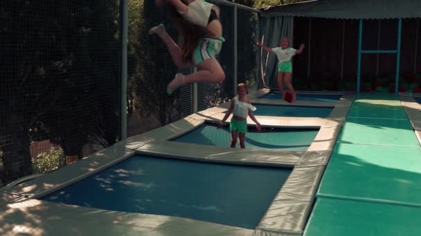 Drei Mädchen springen freudig auf einem Trampolin. Kleine Mädchen springen im Sommer gemeinsam auf einem Trampolin, spielen, lachen und frönen. — Stockvideo