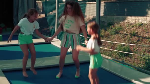 3人の姉妹は喜んでトランポリンでジャンプします。夏の女の子は一緒にトランポリンでジャンプ,遊ぶ,笑うとふける. — ストック動画