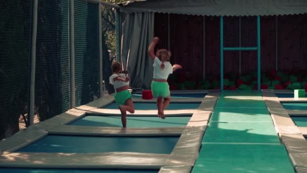 Twee meisjes zussen springen vrolijk op een trampoline. Meisjes in de zomer springen samen op een trampoline, spelen, lachen en verwennen. — Stockvideo