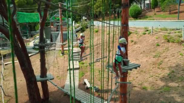 Niños en el parque de cuerdas. Niñas hermanas corren una carrera de obstáculos en un parque de cuerdas . — Vídeos de Stock