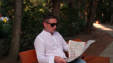 Parktaki ağaçların arka planında çekilmiş bir adamın portresi. Parkta bir adam bankta oturur ve gazetenin sayfalarını karıştırır.