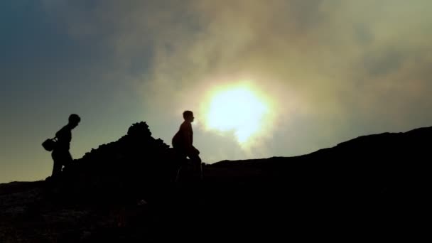 Reizen, mensen wandelen in de bergen. Donkere silhouetten van mensen die in de bergen lopen tegen de achtergrond van de zon die door de wolken schijnt. 4k — Stockvideo