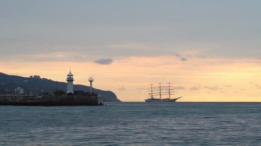 Sabahın erken saatlerinde deniz feneri ve arka planda üç direkli bir gemi denizde sürükleniyor. 4k