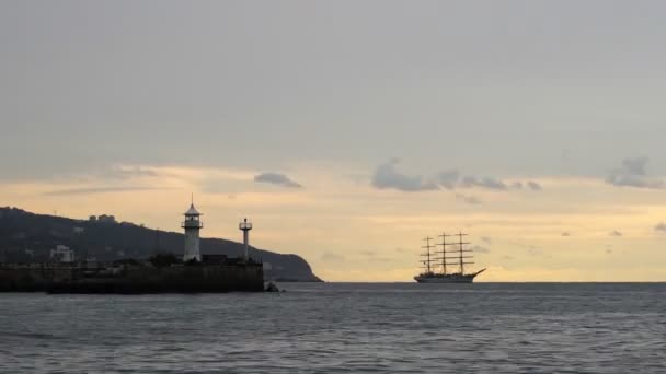 Tijdsverloop. Vuurtoren vroeg in de ochtend en op de achtergrond drijft een driemaster in zee. 4k — Stockvideo