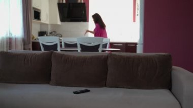 Genç bayan ev hanımı sinirli bir şekilde cep telefonuyla konuşuyor, üzgün bir şekilde kanepede oturuyor ve televizyon izlemeye çalışıyor. 4k