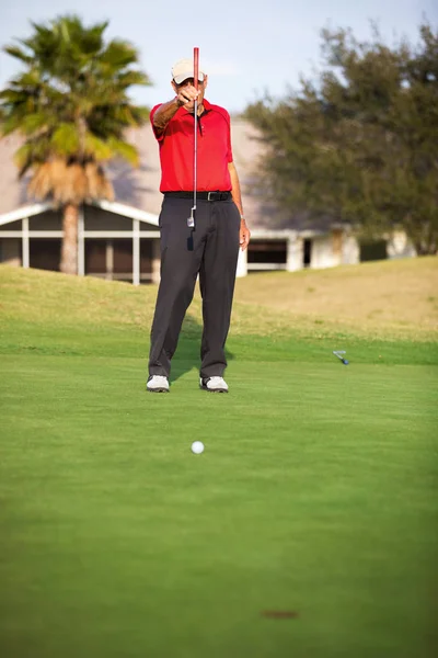 Active senior man lining up a put with hs putter on the green of a golf course resort