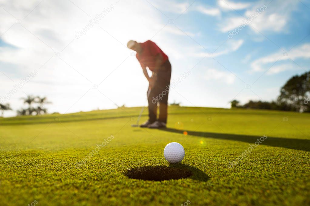 Active senior man puts the ball on golf course green