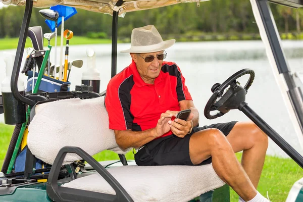 Senior man in golf cart texting on mobile phone.