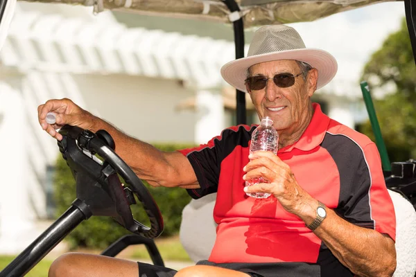 水を飲んでゴルフ カートに座っている年配の男性 — ストック写真