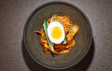 Bibim-guksu pişmiş şehriye, soya sosu, susam yağı, susam tohumu ve şekerle karıştırılmış susam yağında kızartılmış biftek, salatalık turşusu ve mantar içerir. Baharatlı eriştenin üstüne ve etrafına garnitürler konmuş.