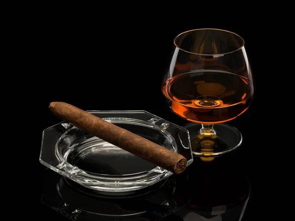 Konyak ve puro siyah izole bir cam kül tablası içinde